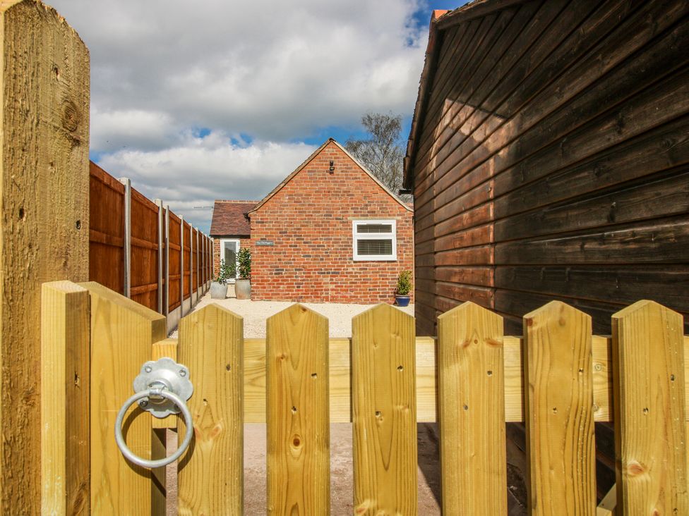 A gate leading to a gravel area with a brick house at The Old Piggery in Ironbridge