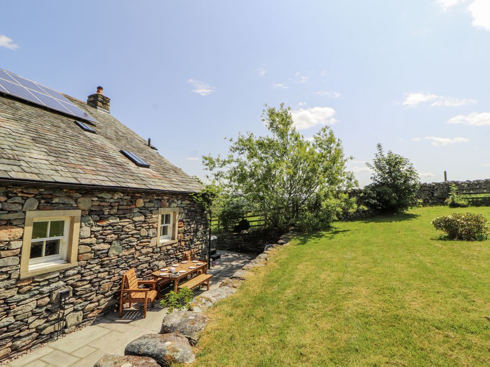 A stone house with a table and chairs in a garden at High Wood Foot, Bampton, Cumbria