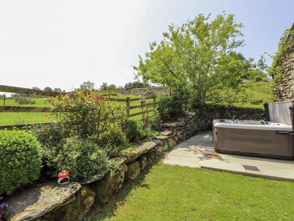 An outdoor area with a hot tub and stone wall at High Wood Foot in Bampton, Cumbria