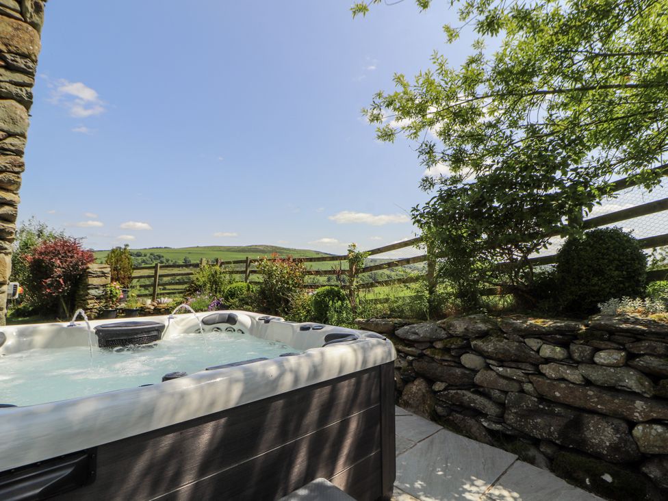 A hot tub next to a stone wall with plants at High Wood Foot in Bampton, Cumbria