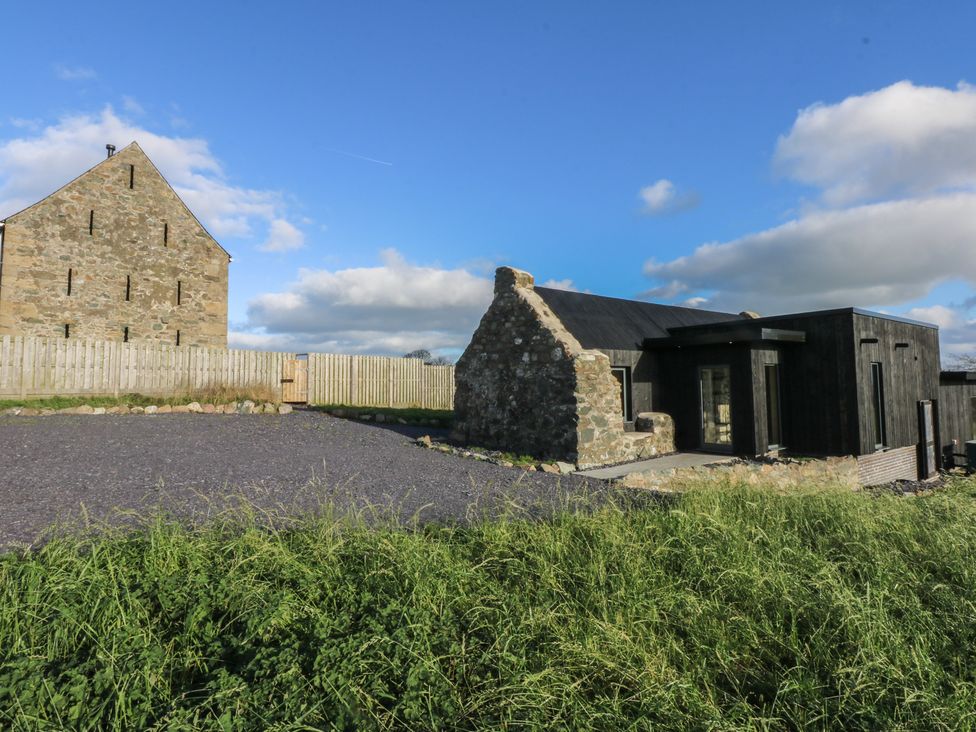 A stone building and a modern structure with fencing at Tithe Barn Lodge Capel Mawr near Malltraeth