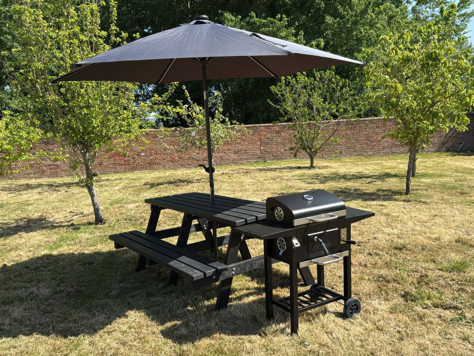 A picnic table with an umbrella and a grill in a garden at Pine Lodge in Bridgwater