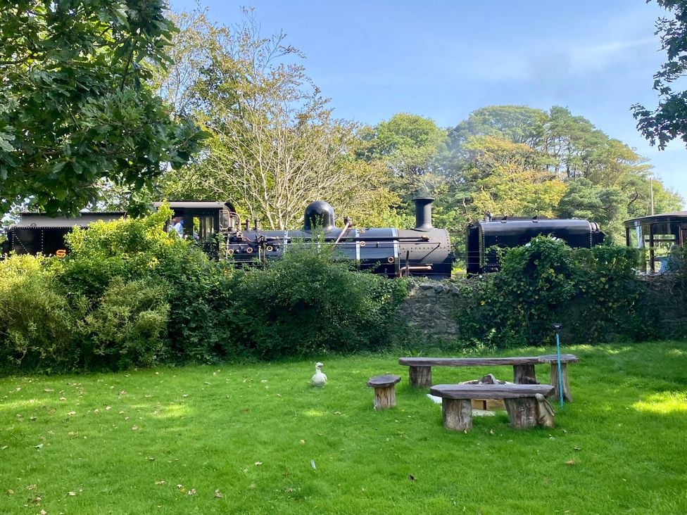 A steam train passing through a garden with a duck and seating area at Garden Flat in Porthmadog