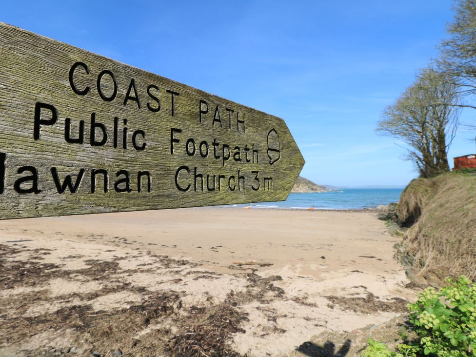 A wooden sign pointing to coast path public footpath and lawnan church next to a sandy beach and sea with trees on the right