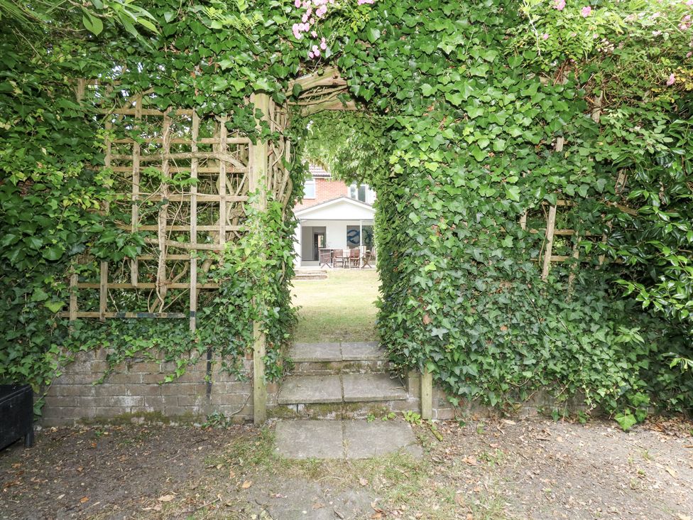 A garden with an archway covered in ivy leading to a table and chairs at King Henry House in Lymington