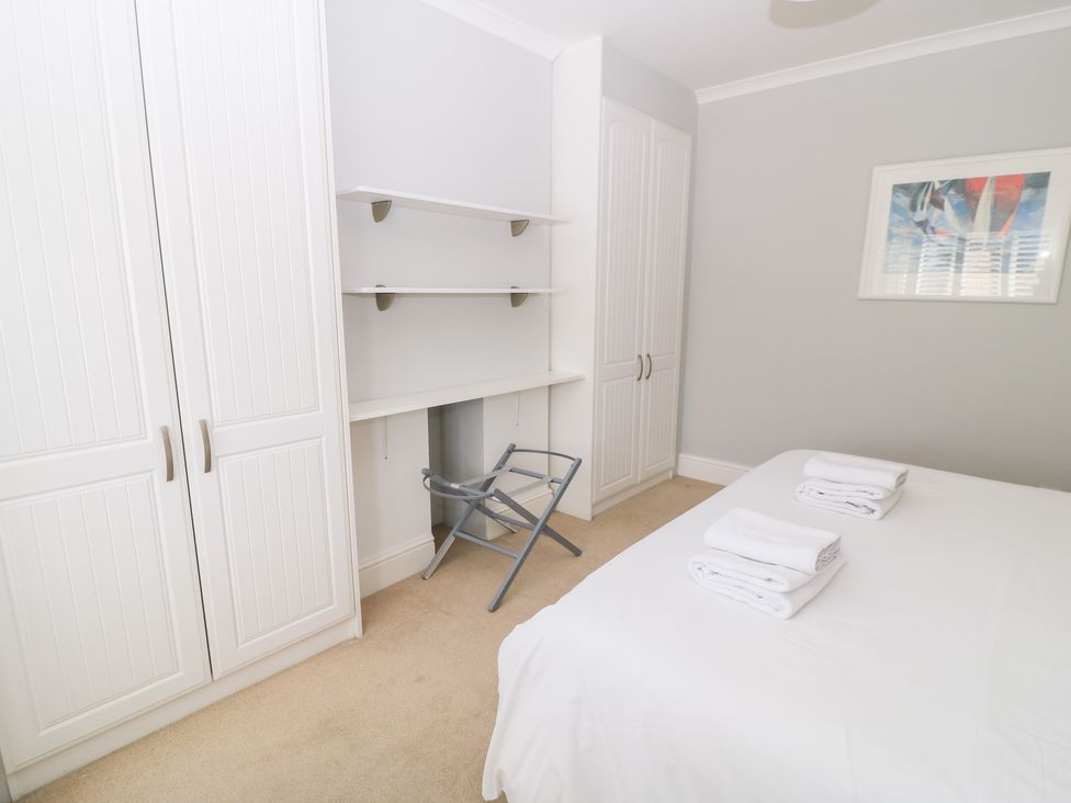 A bedroom with a bed, wardrobe, shelves, and an ironing board at King Henry House in Lymington