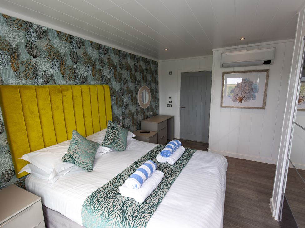 A bedroom with a yellow headboard and towels at Dahlia in Portreath