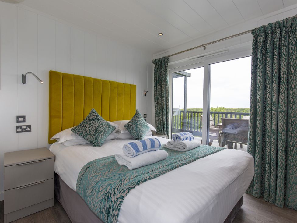 A bedroom with a yellow headboard and large window at Dahlia in Portreath