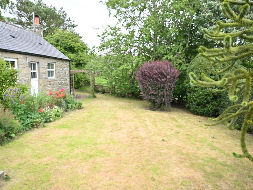 A garden with a stone house and various plants at Petty Knowes Cottage Rochester near Otterburn