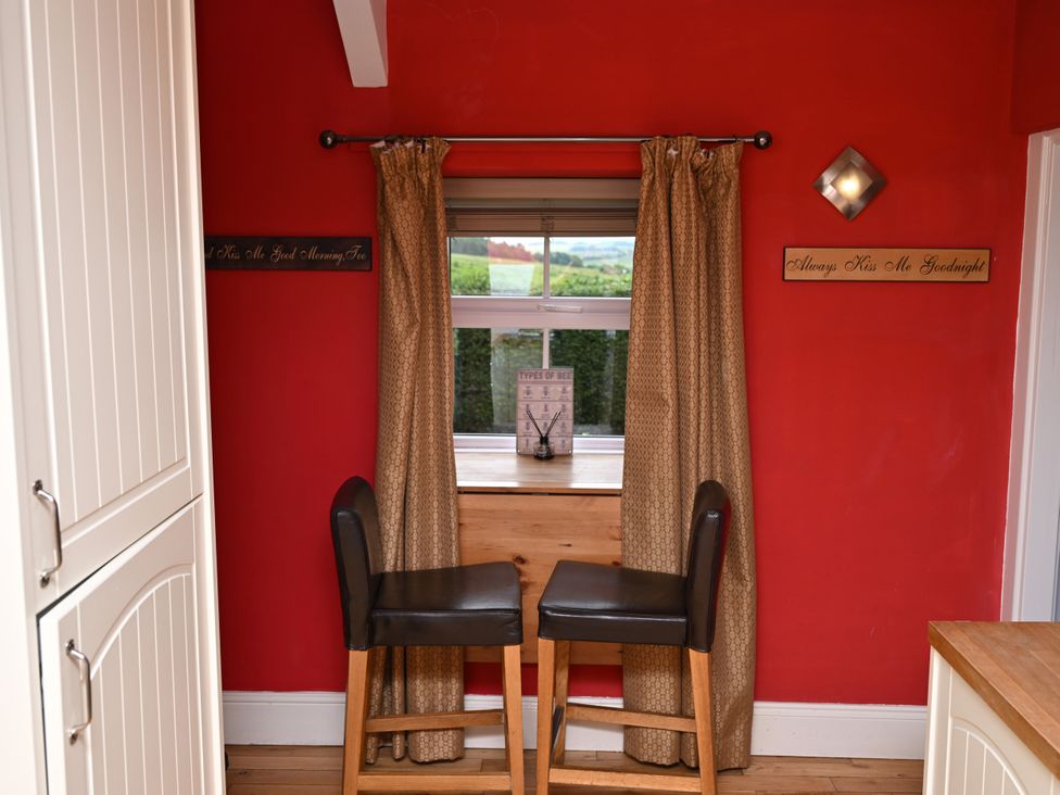 A kitchen with two bar stools and a window at Petty Knowes Cottage, Rochester near Otterburn