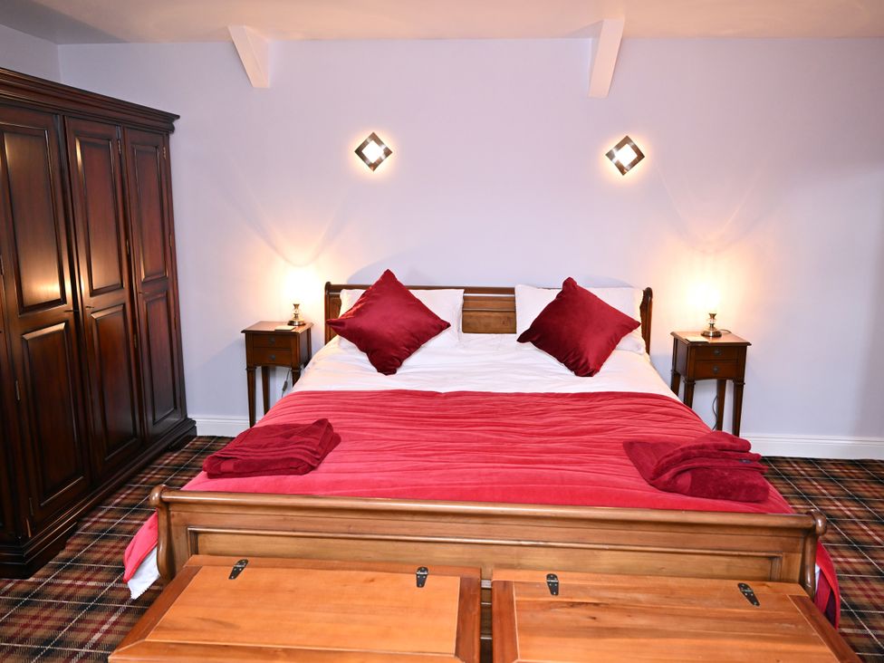 A bedroom with a bed, wardrobe, and bedside table at Petty Knowes Cottage near Rochester