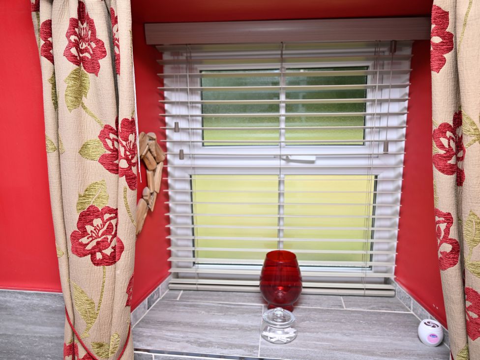 A window with curtains and a red vase at Petty Knowes Cottage Rochester near Otterburn