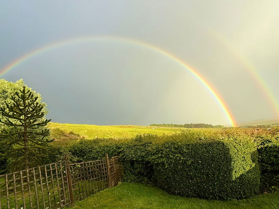 A view with a rainbow over a field and trees at Petty Knowes Cottage in Rochester near Otterburn