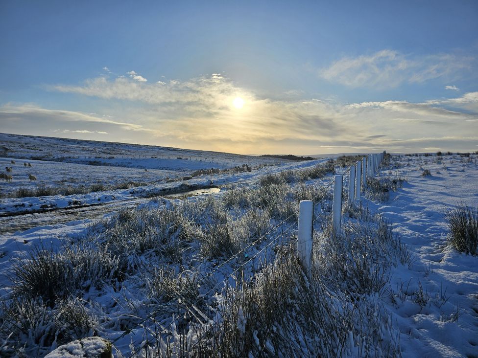 A snowy landscape with a fence and road at Petty Knowes Cottage near Rochester