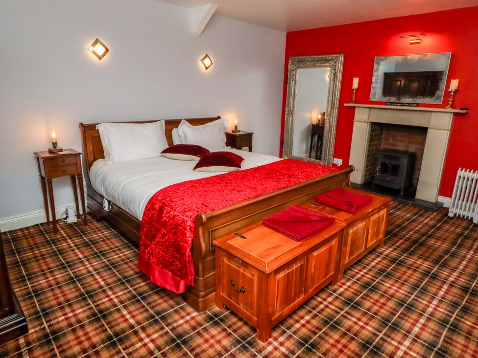 A bedroom with a bed, nightstand, mirror, and fireplace at Petty Knowes Cottage near Rochester