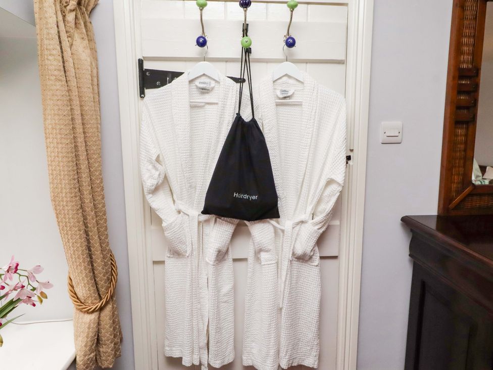 A bathroom with robes and a hairdryer bag hanging on a door at Petty Knowes Cottage Rochester near Otterburn