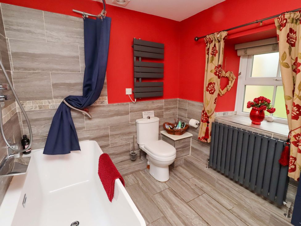 A bathroom with a bathtub, toilet, and window at Petty Knowes Cottage, Rochester near Otterburn