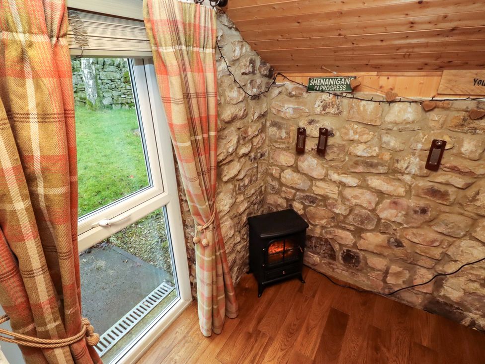 A snug with a window, electric stove, and stone wall at Petty Knowes Cottage in Rochester near Otterburn