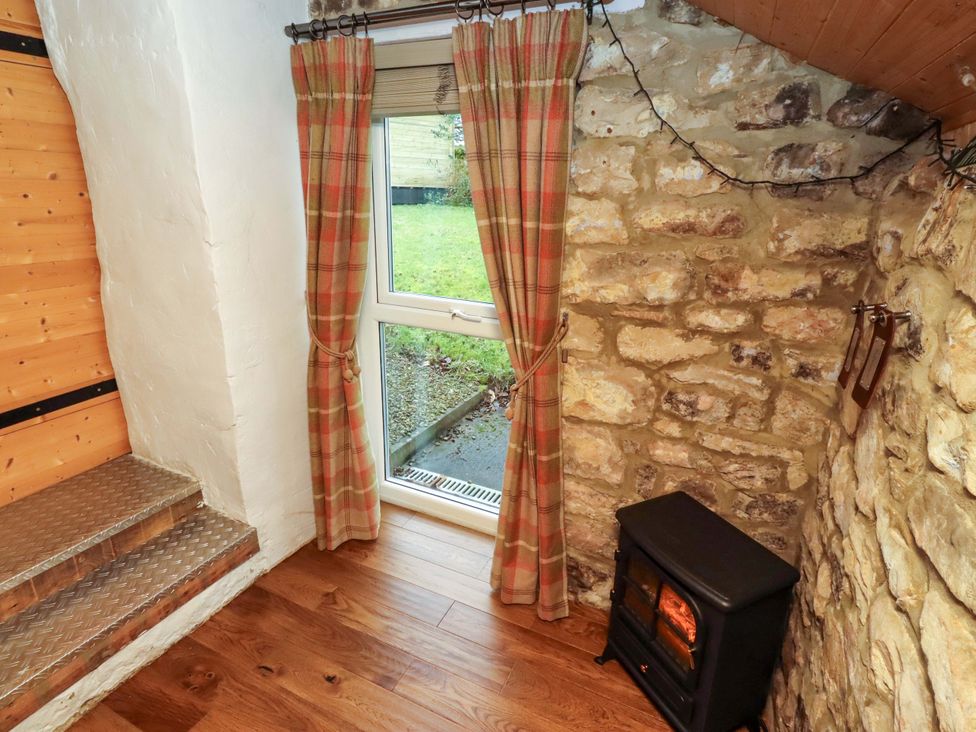 A living room with a window, curtains and a stove at Petty Knowes Cottage Rochester near Otterburn