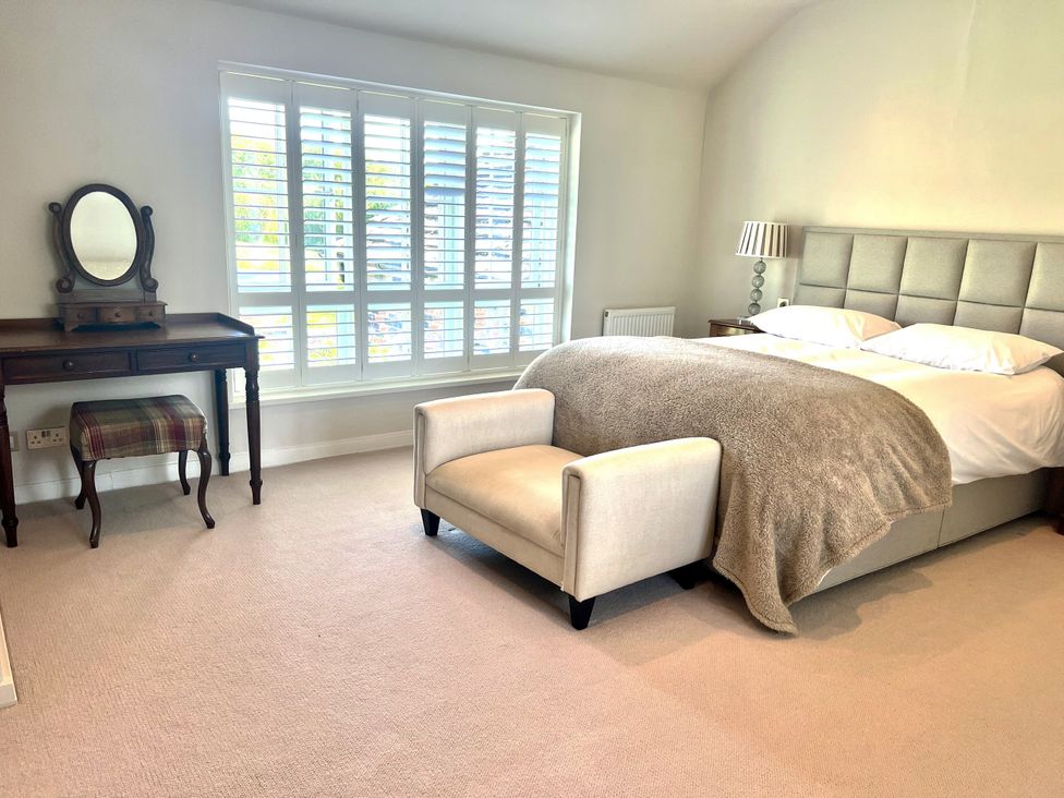 A bedroom with a bed, armchair, and dressing table at Higher Park Farm in Alderley Edge