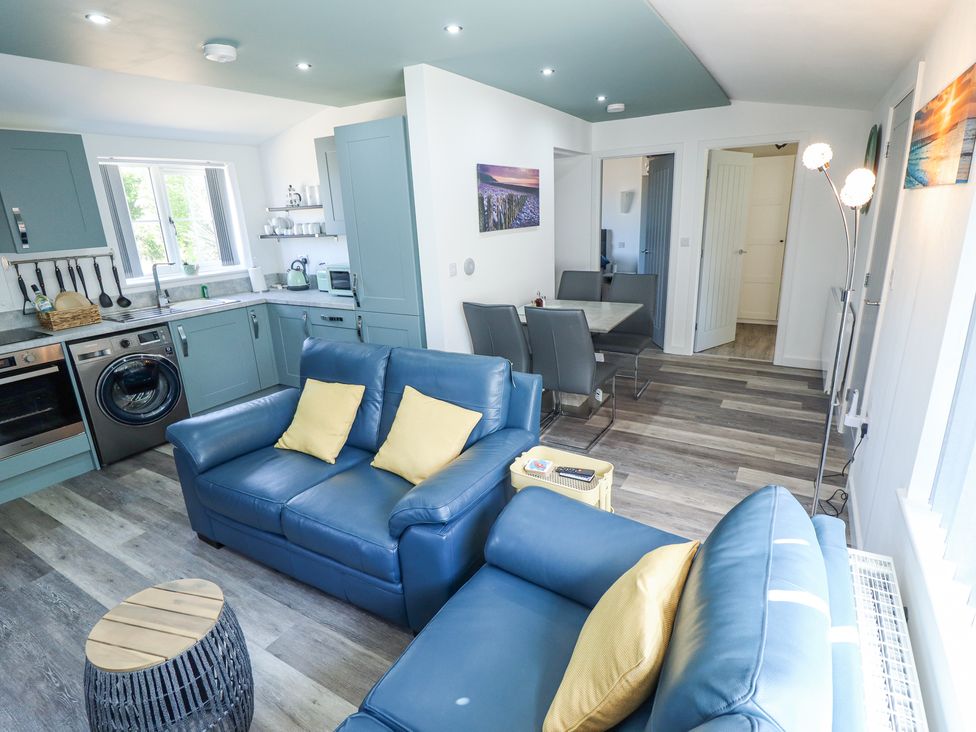 An open plan living room and kitchen with blue sofas yellow cushions dining table and chairs at 19 The Court in Anderby Creek