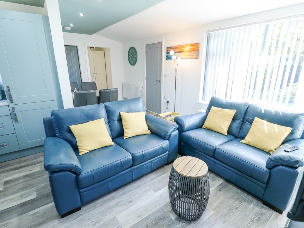 A living room with two blue sofas with yellow cushions a small round table a floor lamp and a wall clock at 19 The Court in Anderby Creek