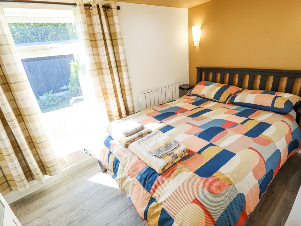 A bedroom with a bed with a colorful geometric bedspread and folded towels by a window with plaid curtains at 19 The Court in Anderby Creek