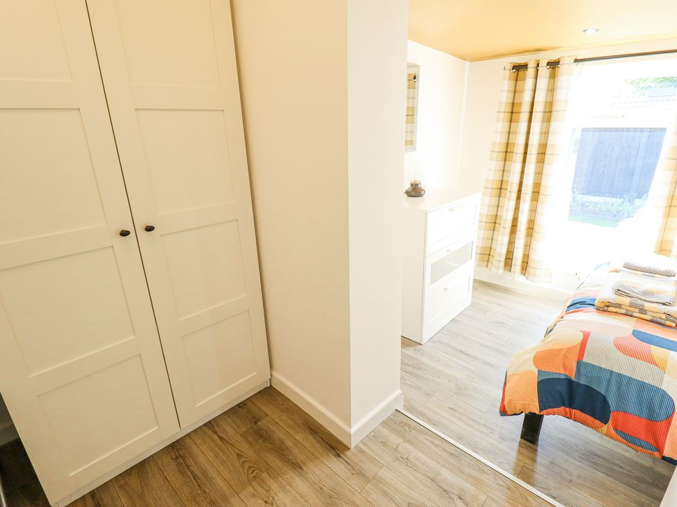 A room with a white wardrobe wooden floor a bed with a colorful blanket and a window with plaid curtains at 19 The Court in Anderby Creek