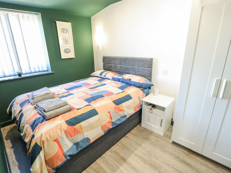A bedroom with a double bed with patterned bedding two folded towels on it a small white nightstand a wardrobe and green and white walls at 19 The Court in Anderby Creek