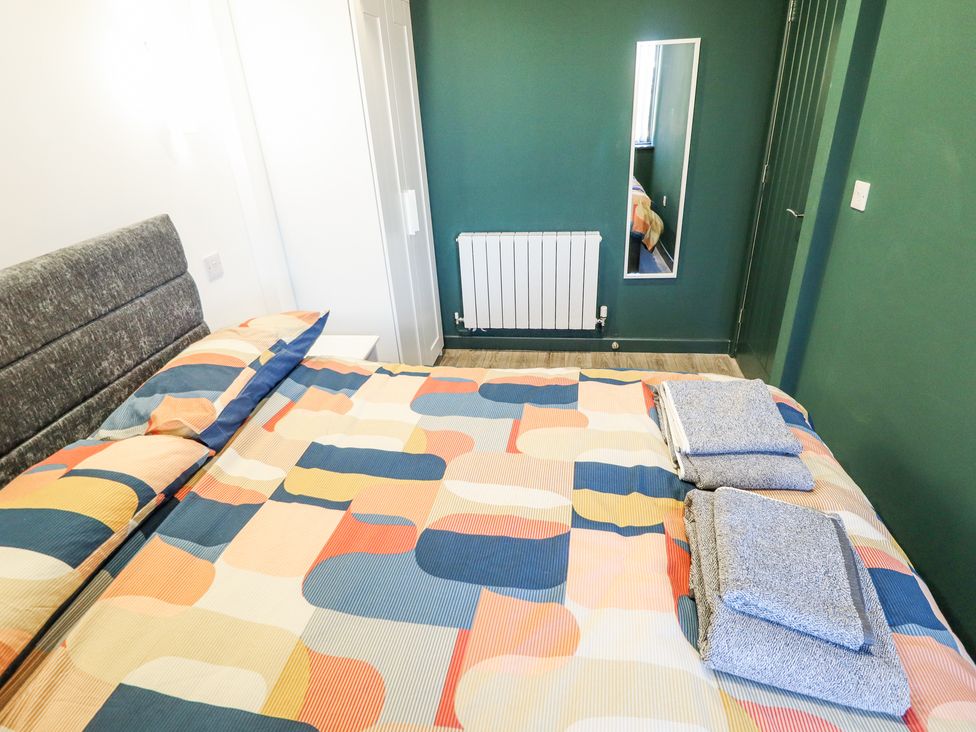 A bedroom with a patterned bedspread blue towels a white wardrobe a wall-mounted radiator and a mirror at 19 The Court in Anderby Creek