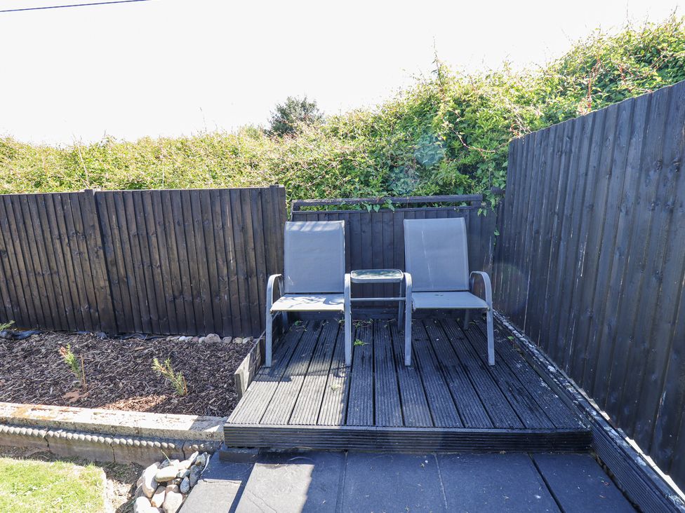 An outdoor seating area with two chairs and a small table on a wooden deck surrounded by dark wooden fencing at 19 The Court in Anderby Creek