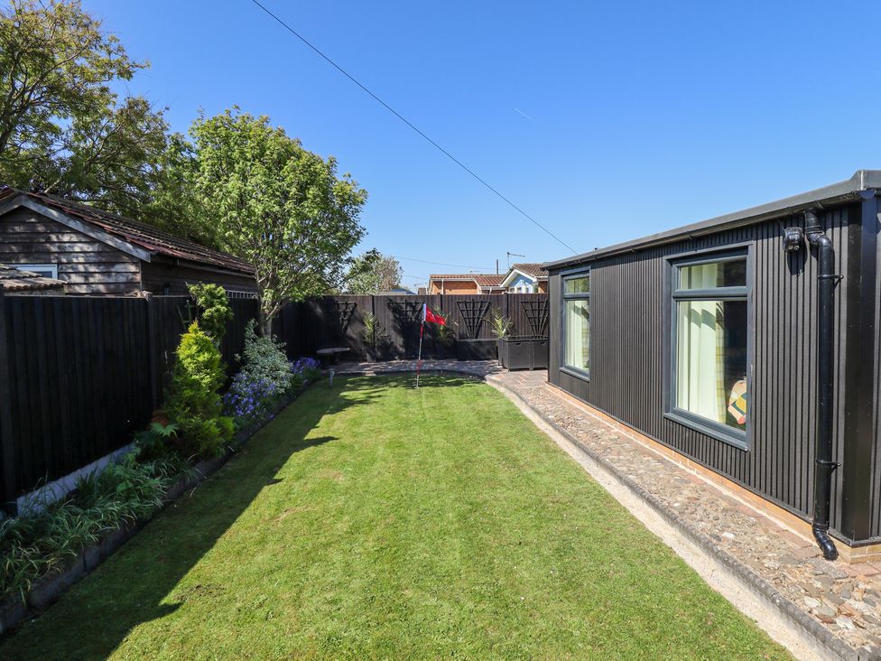 A garden with a lawn and a putting green next to a black wooden building at 19 The Court in Anderby Creek