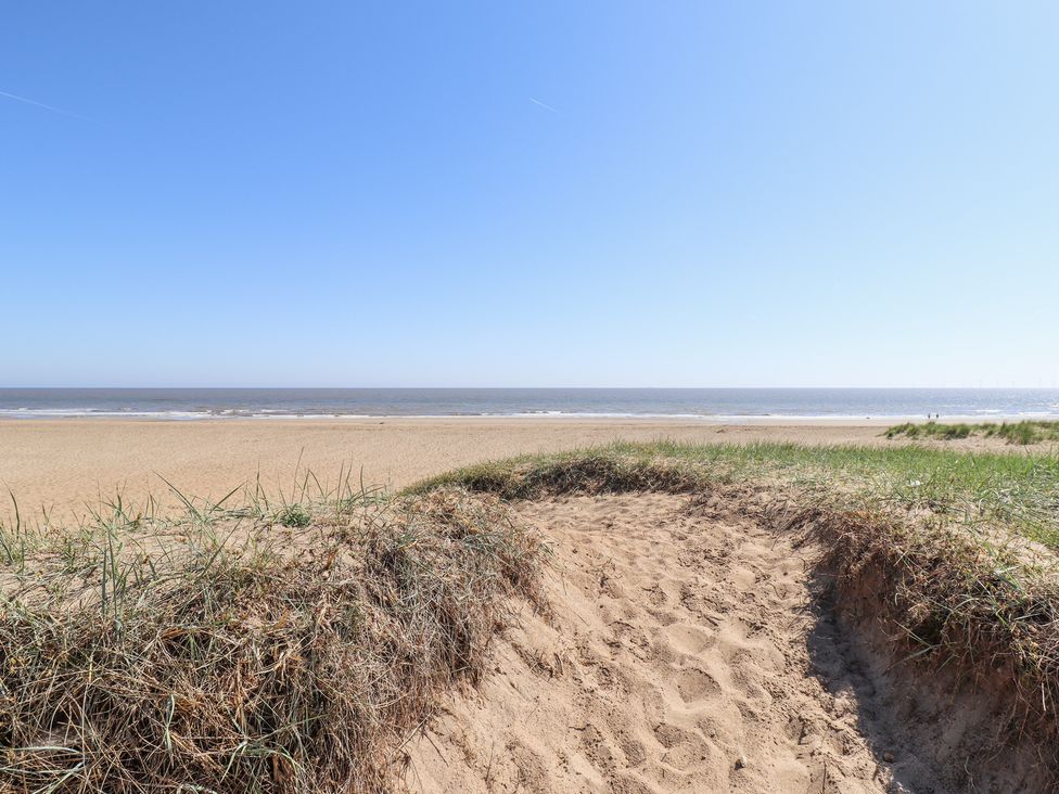 A sandy beach with grass-covered dunes and the sea in the background at 19 The Court in Anderby Creek