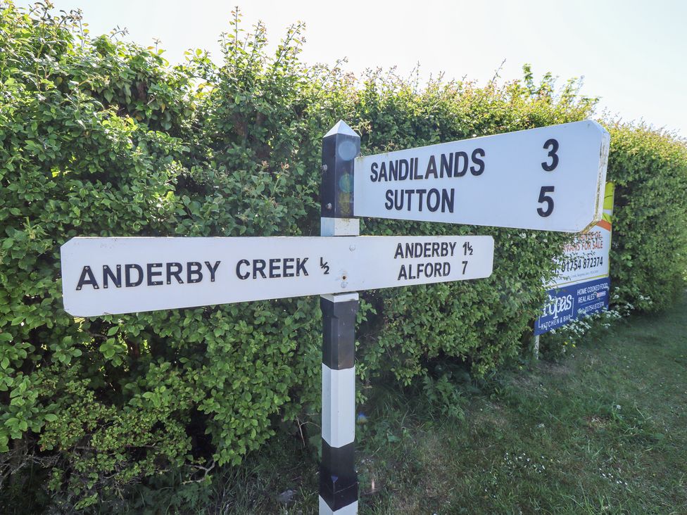 A black and white signpost with directions to nearby locations surrounded by green bushes at 19 The Court in Anderby Creek