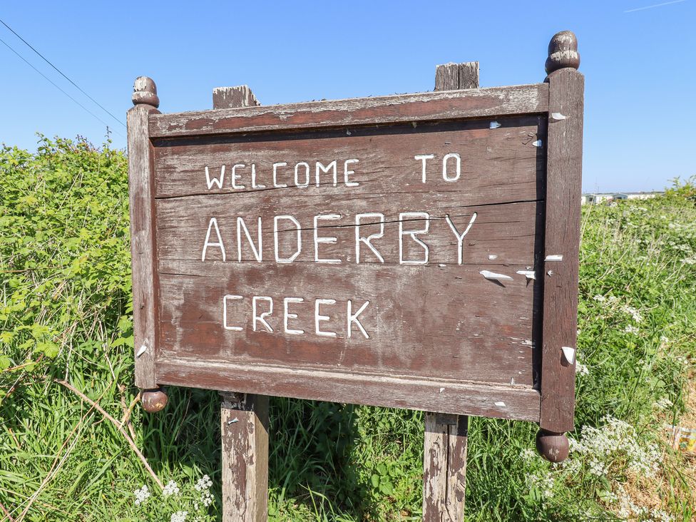 A wooden sign reading welcome to Anderby Creek surrounded by grass and bushes
