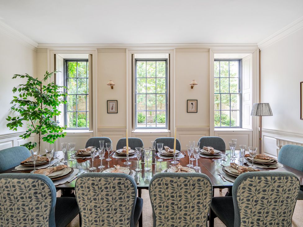 A dining room with a table set and windows at Batheaston House in Batheaston