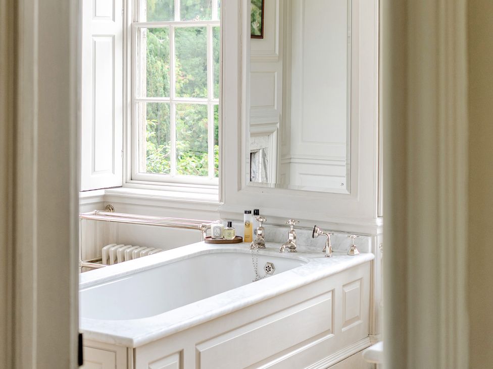 A bathroom with a bathtub and mirror at Batheaston House in Batheaston