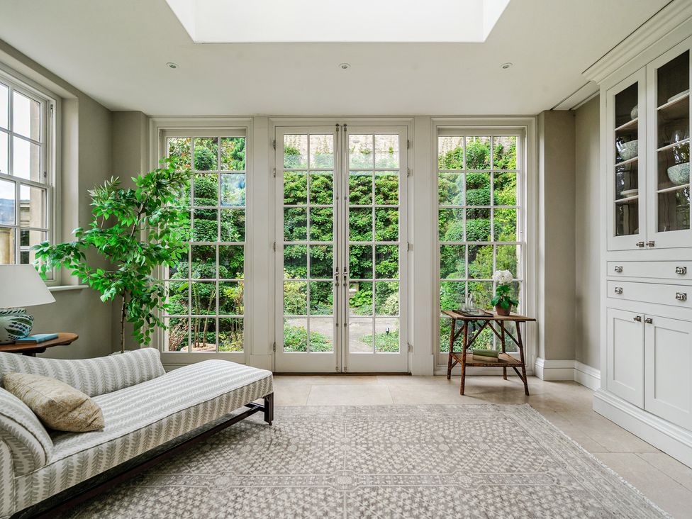A conservatory with a sofa and plants at Batheaston House in Batheaston
