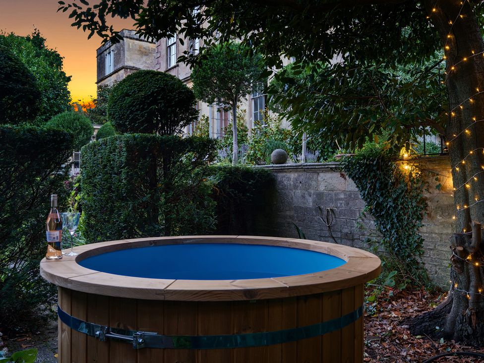 A hot tub with a bottle of wine and glass in the garden at Batheaston House in Batheaston