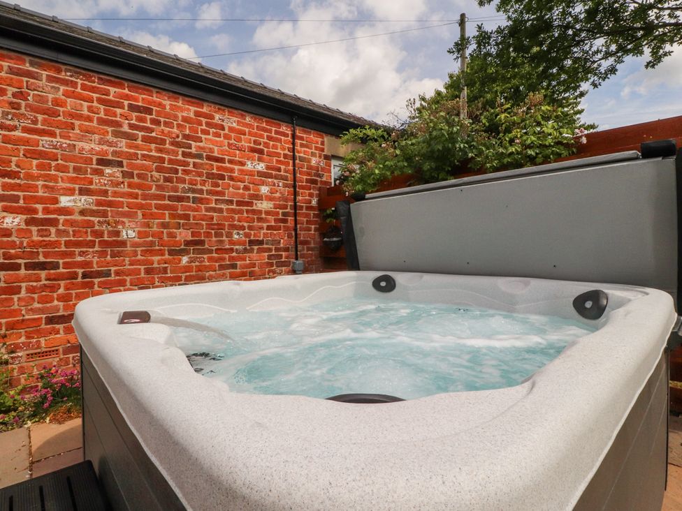 A hot tub next to a brick wall and plants at The Old Coach House in Bilsborrow