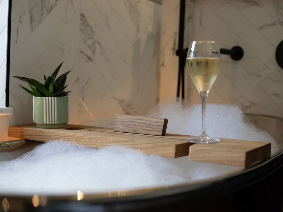 A bathroom with a bathtub, wooden tray, plant and glass at Hilltop Cottage in Conwy