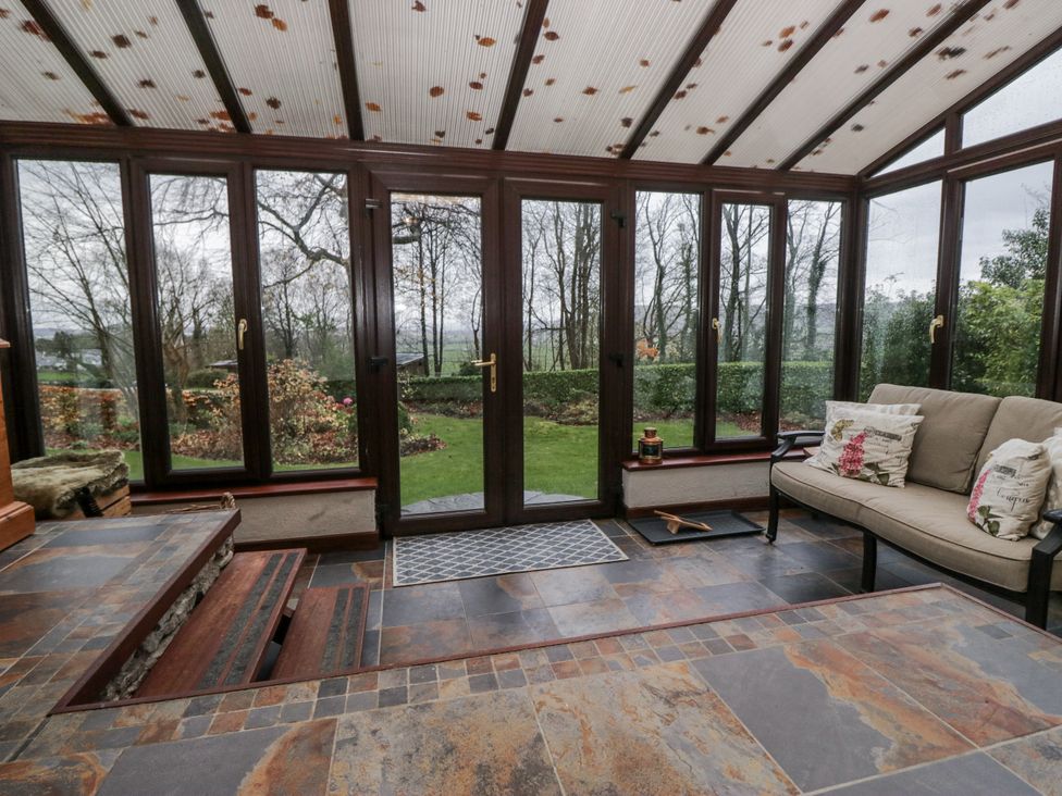 A conservatory with a sofa and door leading to the garden at Beech Brae Kendal