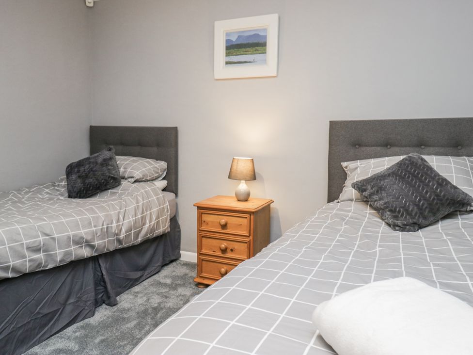 A bedroom with two beds and a lamp on a side table at Beech Brae in Kendal