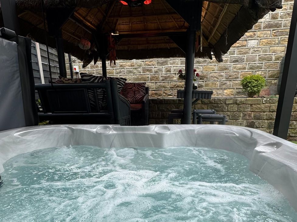 A hot tub with garden seating and a stone wall at Johns Cottage, Harrogate