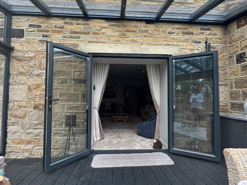 A conservatory with open doors and view into an interior living space at Johns Cottage Harrogate