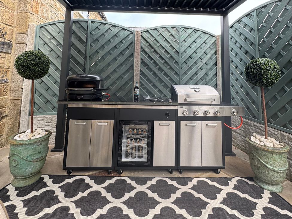 An outdoor kitchen with a grill and refrigerator at Johns Cottage in Harrogate