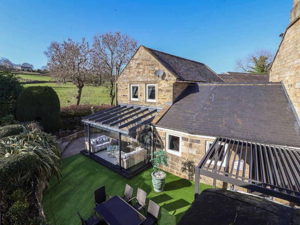 A garden with a glass conservatory and outdoor seating at Johns Cottage in Hampsthwaite