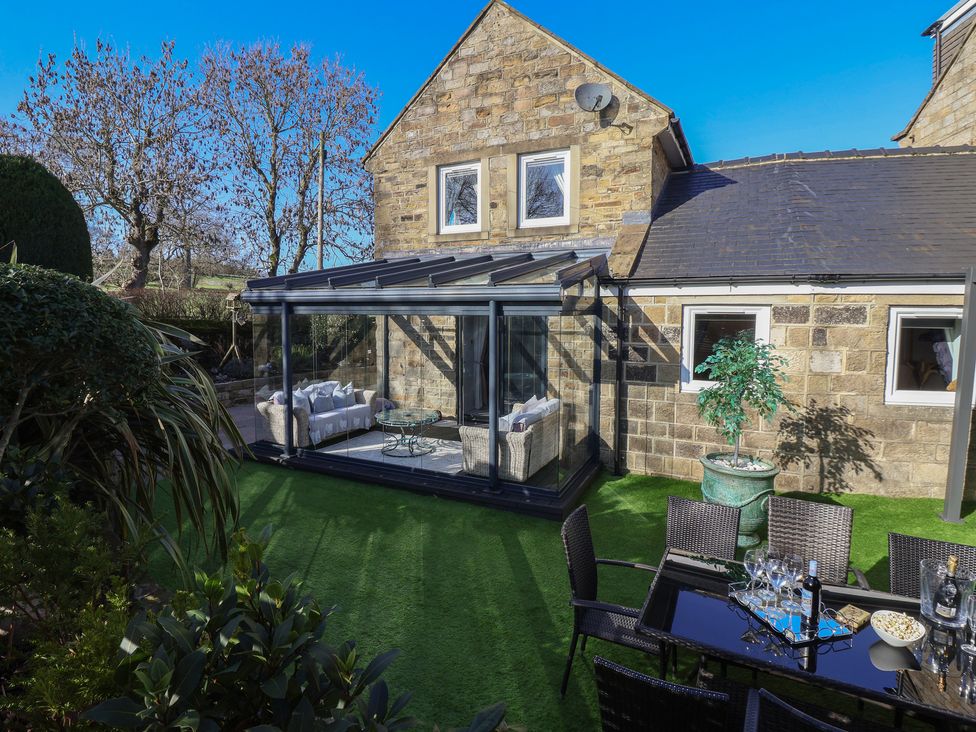 A garden with a conservatory and outdoor dining area at Johns Cottage in Hampsthwaite