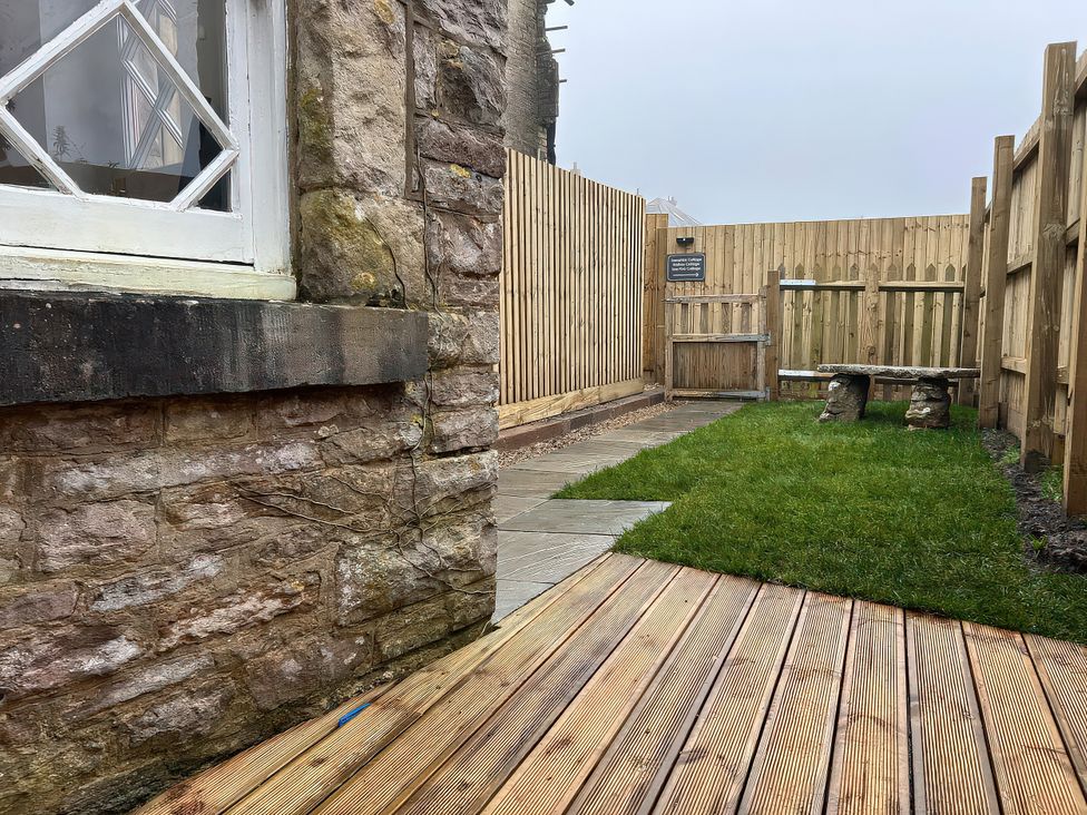 A garden with a stone wall and wooden bench at Sea Pink Studio in Langton Matravers