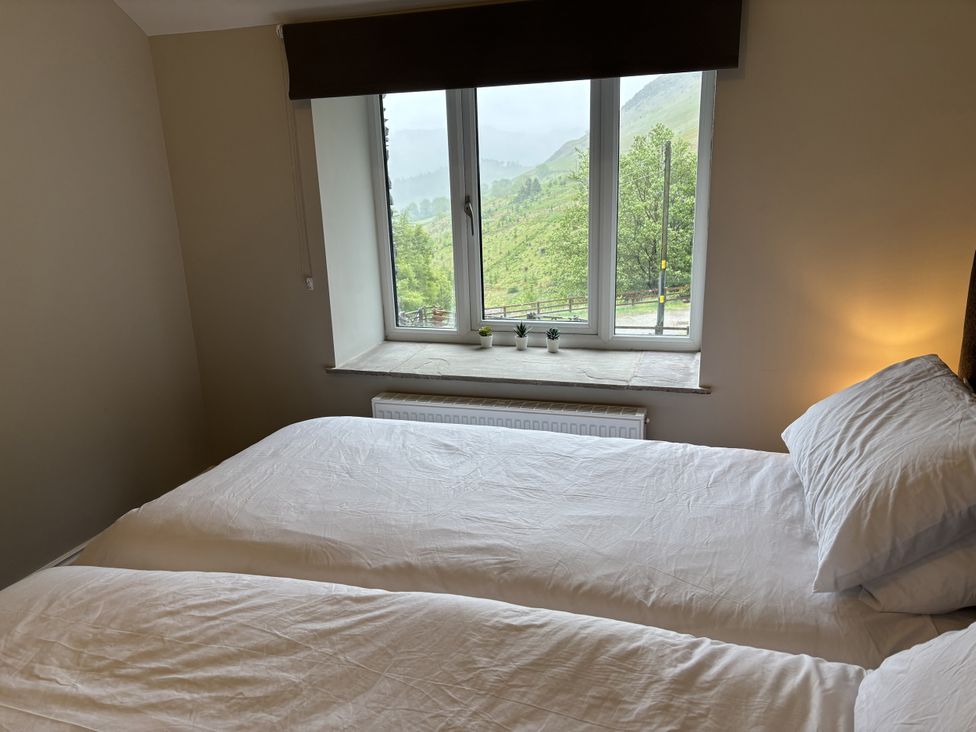 A bedroom with two beds and a window showing a mountain view at Swirral Edge Cottage Glenridding